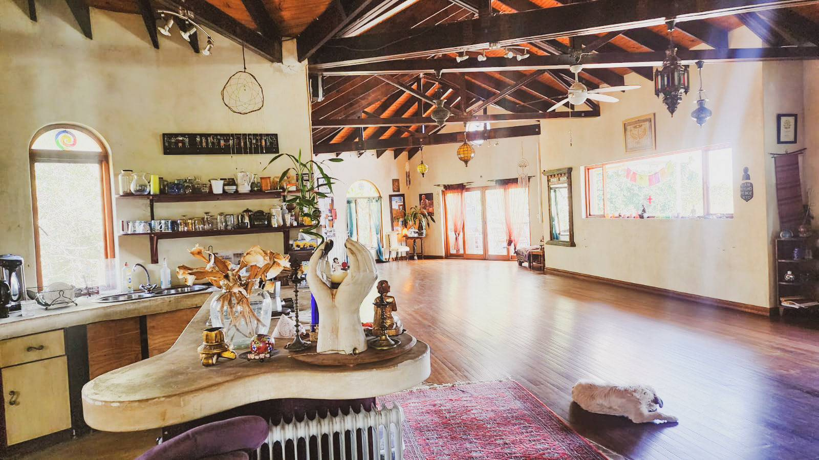 Inside the Eagles View Yoga studio in Gillitts - carved hands and altar pieces on the counter, sunlight across a wide wooden floor beneath high timber beams